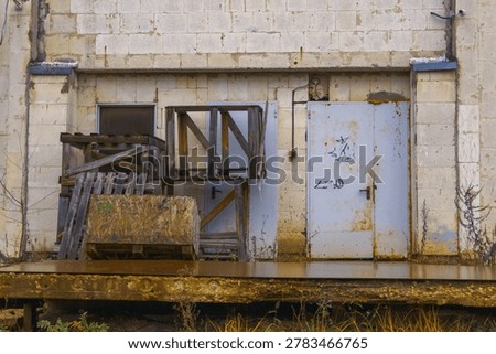 Rusted loading platform with stacked pallets, chained hook, bolted hinges, rotting wood, machine parts, faded markings, industrial service zone left to time