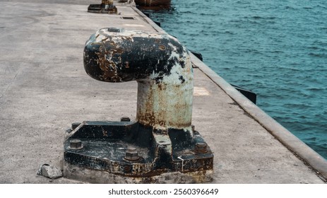 A rusted metal anchor is sitting on a pier. The water is calm and the pier is empty - Powered by Shutterstock