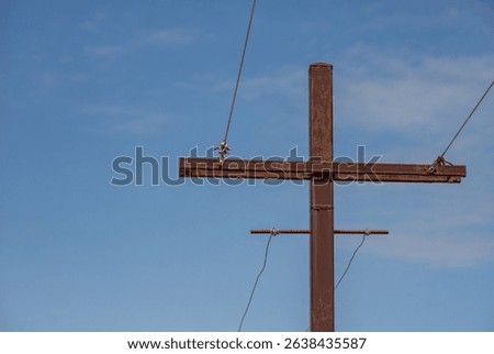 A rusted metal pole with a cross on top of it. The pole is surrounded by wires and is located in a blue sky
