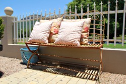 A Rusted Metal Seat Covered In Cushions In A Garden Setting .