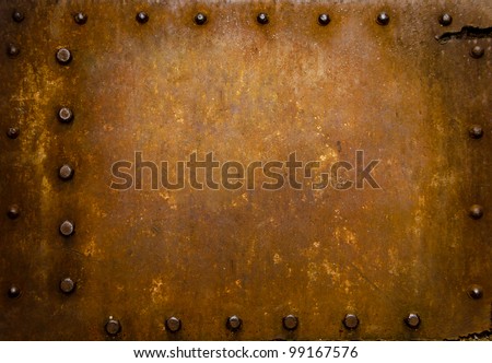 Rusted metal wall plate with three borders of metal studs, showing orange and brown scratch and scuff marks.  Suitable for wallpaper or background or grunge texture.
