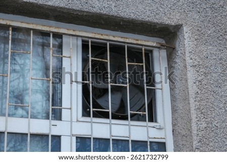 Rusted Security Bars Protecting Window With Industrial Exhaust Fan Inside Concrete Building Wall