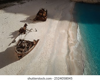 A rusted shipwreck on the sandy beach of Navagio in Zakynthos, Greece, with towering cliffs and a clear blue sky. - Powered by Shutterstock