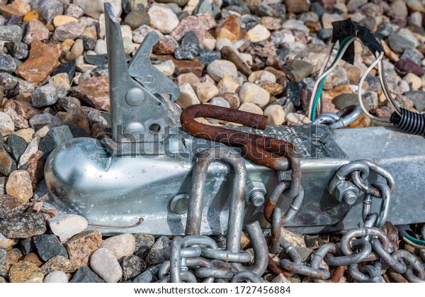 Rusted trailer ball hitch with security chain\
sitting on gravel