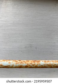 A Rusted Weathered Metal Bar In Front Of A Gray Painted Wooden Wall