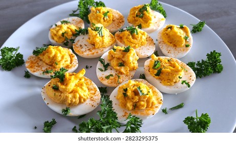 Rustic 1970s style deviled eggs filled with a spoon and garnished with spices and freshly chopped parsley. Close-up of homemade curried eggs with a creamy hand-blended filling, topped with herbs for a vintage party appetizer. 1970s vibe nostalgia food for blogs, mid-century cooking groups, or lifestyle magazines looking for authentic comfort food imagery. Imperfect, spooned-in devilled or curried egg filling oozing homemade, old-school charm that people associate with comfort food, making it stand out from hyper-polished commercial studio shots.