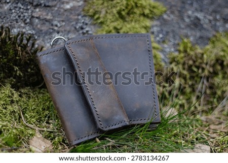 Rustic accessories close-up on a forest background. Crazy Horse vintage leather key case and bifold. Perfect for banners, homepages, social media, gift ads, business and craft articles.