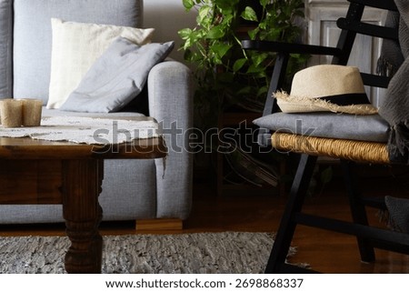 Rustic apartmen room interior featuring a straw hat resting on a wooden chair with a woven seat next to a sofa and coffee table. Horizontal real picture
