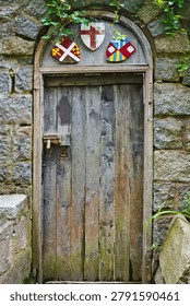 Rustic arched door features weathered wooden planks set within a sturdy, rough-hewn stone wall Gloucester MA USA