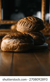 Rustic artisan bread loaves stacked on cutting board on wooden table. Dark moody bakery still life with warm light and vintage background.
