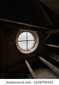 Rustic attic interior with round stained glass window and wooden beams. Vintage architecture, historic building, moody lighting, old house attic, medieval window, natural textures.