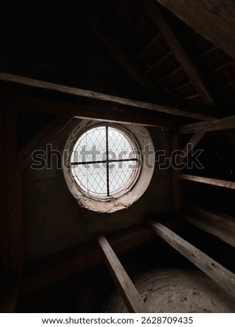 Rustic attic interior with round stained glass window and wooden beams. Vintage architecture, historic building, moody lighting, old house attic, medieval window, natural textures.