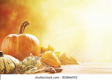 A rustic autumn still life with pumpkins and golden leaves on a wooden surface. Bright sunlight coming in from behind.
