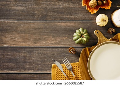 Rustic autumn table setting with empty plate, cutlery, pumpkins, nuts, and candle on wooden background. Perfect for Thanksgiving, harvest, or seasonal food themes.