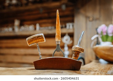 Rustic bar tool set with antler-style handles including corkscrew, bottle opener, and pourer, displayed on a wooden stand in a cozy cabin interior.