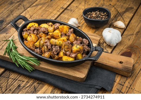 Rustic beef hash with golden fried potatoes served in a cast iron pan on a wooden table, seasoned with garlic, pepper and rosemary