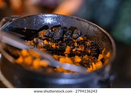 A rustic black pot holds cooked mopane worms with diced carrots in warm indoor light near Victoria Falls, Zimbabwe. Tight composition and shallow depth of field show texture.