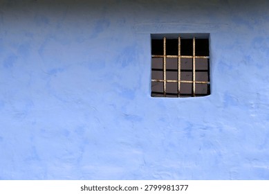 Rustic blue plastered wall with small barred window and weathered iron bars