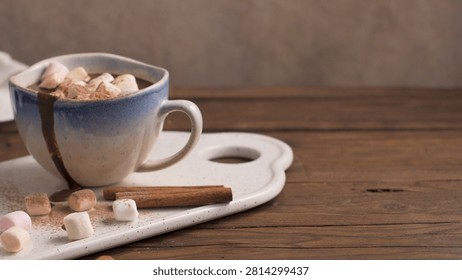A rustic blue and white ceramic mug overflows with rich hot cocoa and mini marshmallows. Soft warm light showcases the powdery cocoa dusting and textured wood surface.