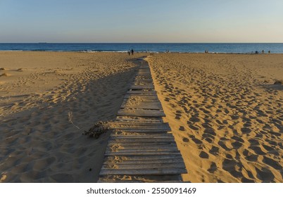 A rustic boardwalk stretches across the sandy beach, inviting visitors toward the calm, shimmering sea. - Powered by Shutterstock