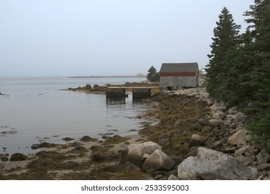 A rustic boathouse near Peggy's Cove, Nova Scotia, with a rocky shore, calm waters, and a cloudy sky. - Powered by Shutterstock