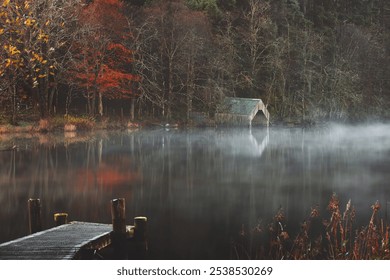 A rustic boathouse reflects in the misty, tranquil waters of Loch Ard, creating an eerie yet serene autumnal scene in Aberfoyle, Scotland. - Powered by Shutterstock