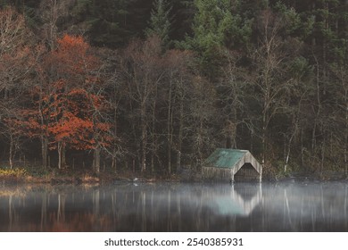 A rustic boathouse reflects in the misty, tranquil waters of Loch Ard, creating an eerie yet serene autumnal scene in Aberfoyle, Scotland. - Powered by Shutterstock