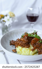 Rustic Braised Beef Stew  - Boeuf Bourguignon - with Mashed Potatoes and Glass of red Wine and Fresh Herbs in a Cozy Setting