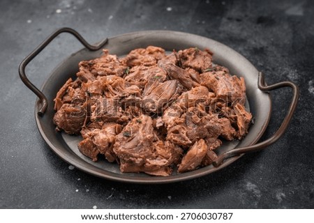 Rustic braised moose venison stew, shredded and savory, plated with fresh rosemary on a metal dish over dark stone background.