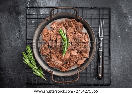 Rustic braised moose venison stew, shredded and savory, plated with fresh rosemary on a metal dish over dark stone background.