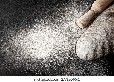 Rustic bread loaf with flour and rolling pin on dark background