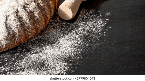 Rustic bread loaf with flour and rolling pin on dark background