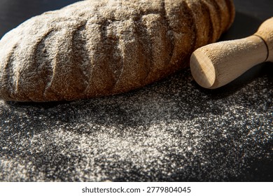 Rustic bread loaf with flour and rolling pin on dark background