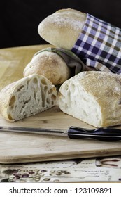 Rustic bread wrapped in kitchen towels with one sliced on a cutting board