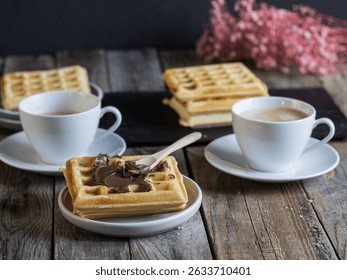 Rustic breakfast setup with coffee and waffles topped with chocolate spread, served on a wooden table in a cozy, home-style atmosphere.