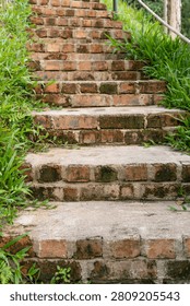 A rustic brick staircase surrounded by lush green vegetation leads uphill through a peaceful garden, highlighting weathered textures and a natural outdoor setting.