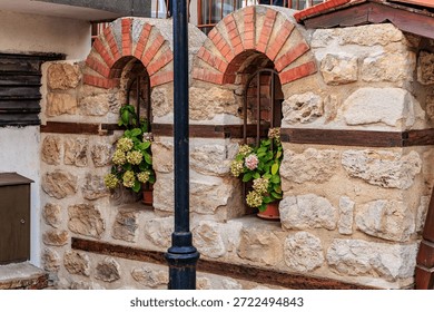 Rustic brick and stone wall with arched windows and floral decor.