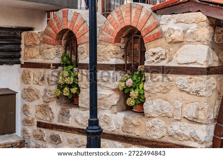 Rustic brick and stone wall with arched windows and floral decor.