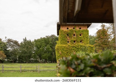 A rustic brick tower is covered in lush green ivy, standing in a meadow. Its small windows and climbing plants give it a timeless charm.