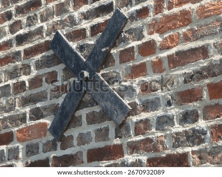 Rustic brick wall features a prominent cross-braced support that appears weathered from time, indicating structural reinforcement in a historic setting.