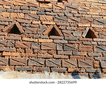 Rustic brick wall with triangular ventilation openings and diagonal carved patterns.
