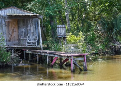 Rustic Cabin In The Bayou Swamp With Cistern, Traps, Wicker Chair And Red Dock