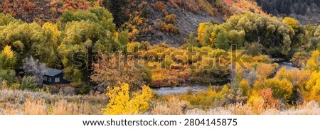 Rustic cabin surrounded by colorful fall foliage along winding river in wilderness landscape in Utah
