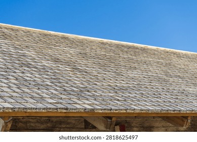 Rustic cedar shake roof texture background with repeating pattern of old wooden tiles. Detailed texture of traditional weathered wooden shingle roof against clear blue sky