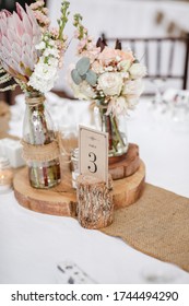 Rustic centrepiece setting on table at wedding with jar of King Protea and hydrangeas and wood rounds. Selective Focus