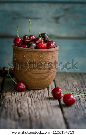 Rustic ceramic cup, full of fresh picked cherries on a old wooden table.