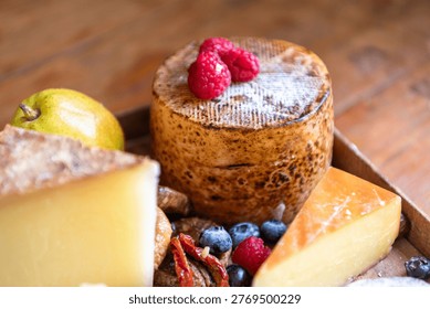 A rustic cheese platter featuring various cheeses, raspberries, blueberries, and a pear on a wooden surface.
