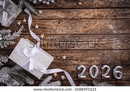 Rustic Christmas background with gift boxes tied with white ribbon and snow fir branches on vintage wooden table. Ideal for holiday cards, seasonal banners, and festive designs. 2026