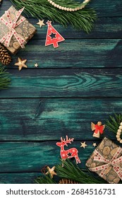 Rustic Christmas flat lay with pine branches, pinecones, wooden stars, and beads on teal wood table. Top view, Xmas vertical background.