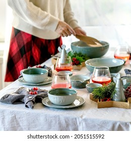 Rustic Christmas Table Setting With Empty Craft Ceramic Tableware, Plates And Bowls, Xmas Angel Decorations On White Tablecloth In Front Of The Window. Woman Hold A Salad Bowl. Square Image